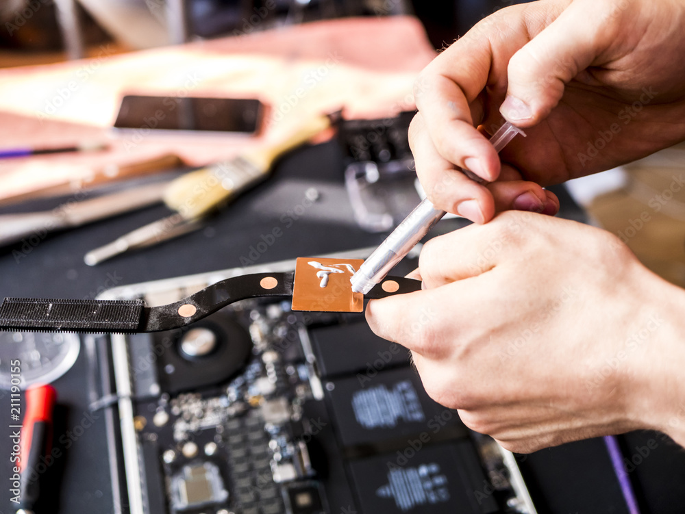 hands with thermal paste applying it to the computer laptop chip