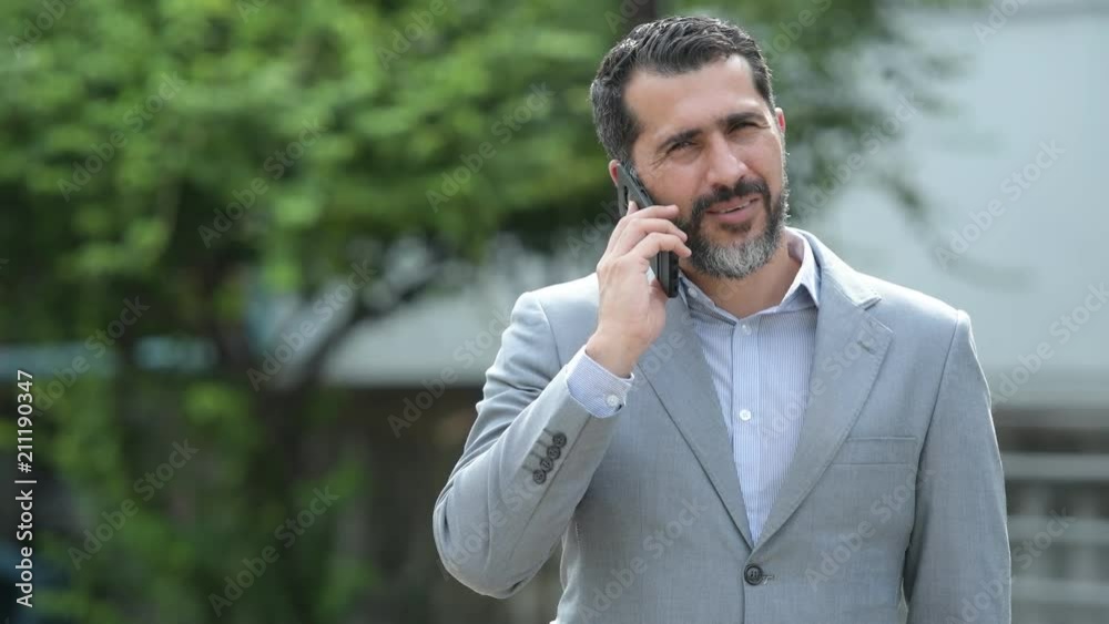 Handsome Persian bearded businessman talking on phone in the streets outdoors Handsome Persian bearded businessman talking on phone in the streets outdoors