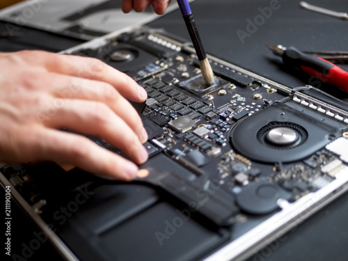 Tableau sur toile hand with brush clearing the disassembled laptop from dust and dirty close up in