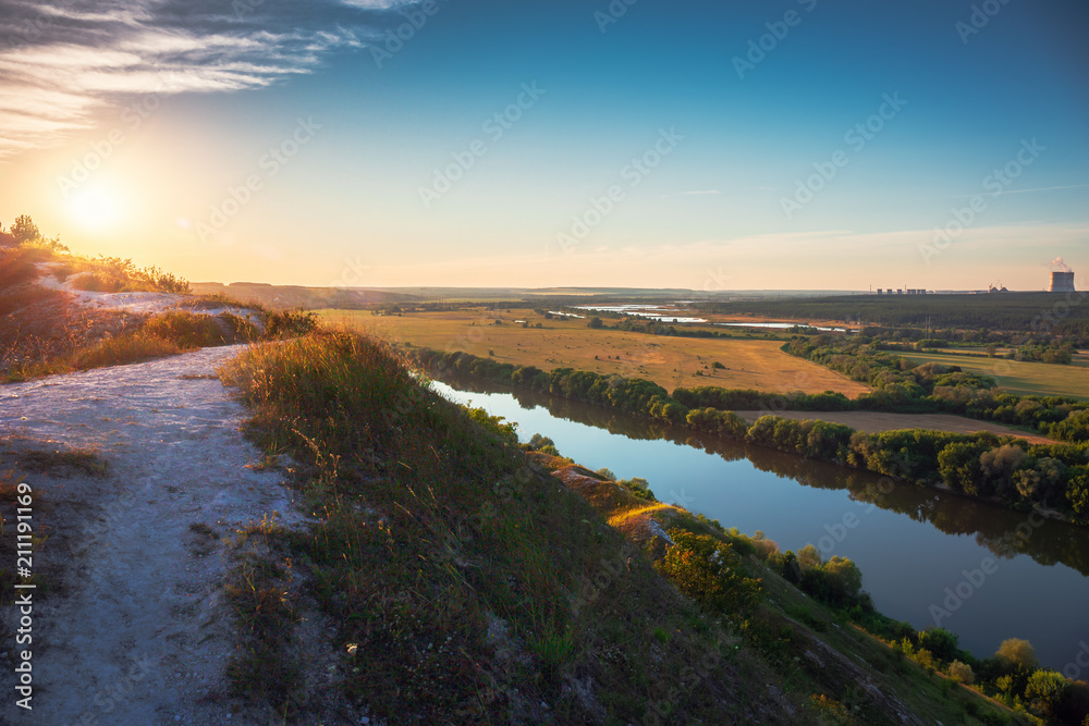 Beautiful nature landscape panorama at sunset time. View from chalk hill or mountain to green meadows and fields with river and nuclear power plant far away. Summer travel tranquil background