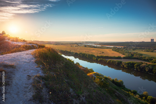 Beautiful nature landscape panorama at sunset time. View from chalk hill or mountain to green meadows and fields with river and nuclear power plant far away. Summer travel tranquil background © DedMityay