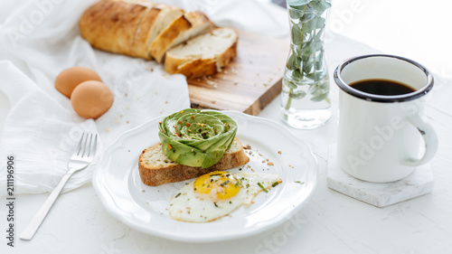Breakfast setting featuring avocado rose on toast  sunny side up egg and coffee.
