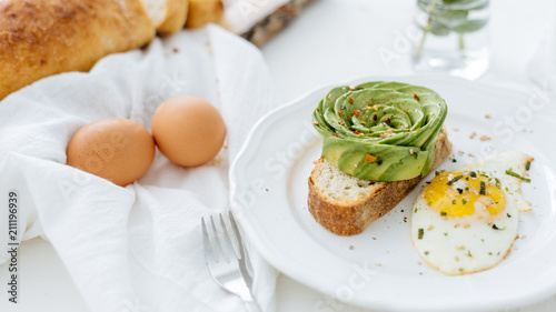 Breakfast setting featuring avocado rose on toast, and sunny side up egg.