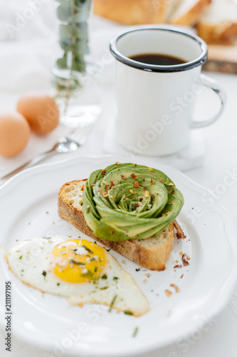 Breakfast setting featuring avocado rose on toast, sunny side up egg and coffee.