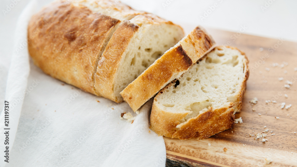 Loaf of bread sliced on wood cutting board and white linen.