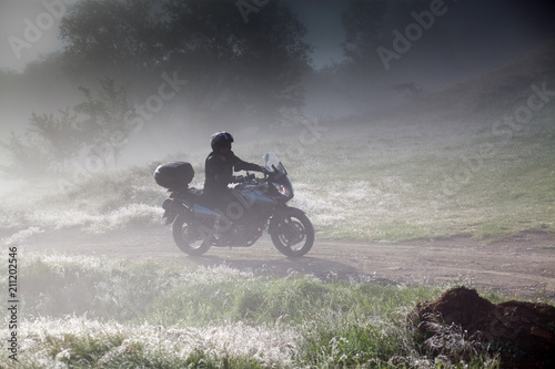Fototapeta Naklejka Na Ścianę i Meble -  silhouette of a man riding a motorbike on foggy road in early morning