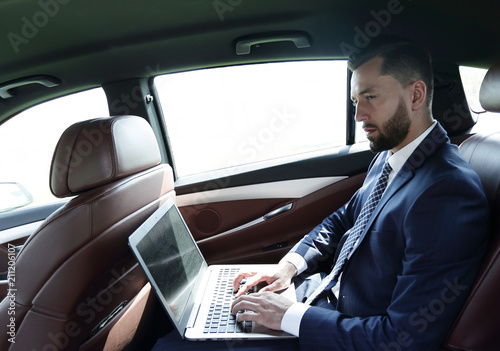 businessman using a laptop in the backseat of a car © ASDF