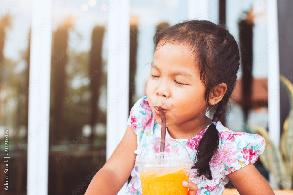 Cute asian little child girl drinking orange juice in plastic glass with a straw in the restaurant Cute asian little child girl drinking orange juice in plastic glass with a straw in the restaurant