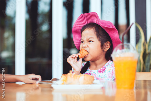 Cute asian little child girl eating delicious toast and orange juice for breakfast with happiness
