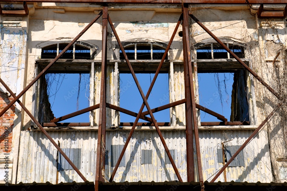 Facade of a derelict building supported by rusty iron scaffolding.