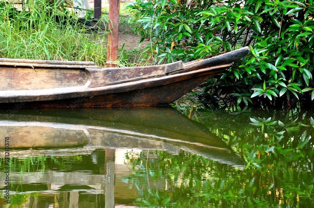 Bow of an old wooden boat moored against a grassy bank, showing a perfect mirror image reflection in the water Bow of an old wooden boat moored against a grassy bank, showing a perfect mirror image reflection in the water