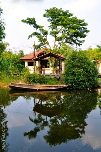 Wooden boat moored in front of a small basic home on a traditional rural canal in Asia