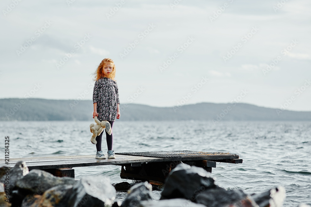 A lonely girl with a plush Bunny is standing on the pier and loo