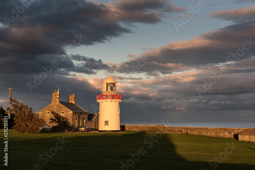 Vászonkép Ballinacourty lighthouse lit by the setting sun with the sea and dark clouds in the background