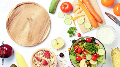 Top view of empty wooden plate, mixed vegetables salad, muesli and fresh fruits on white background.