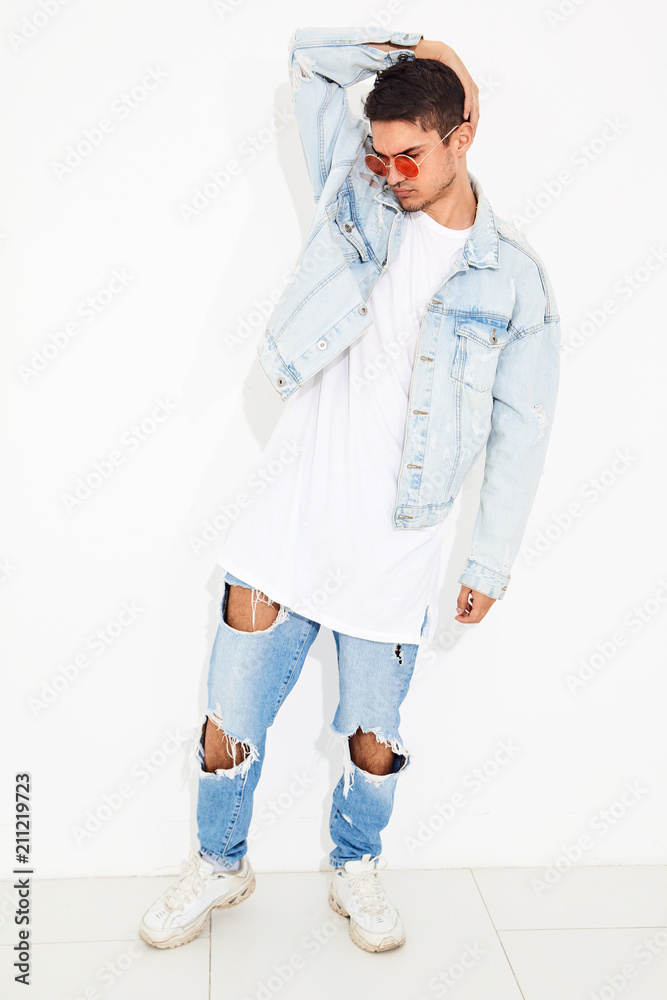 Portrait of handsome young model man dressed in jeans clothes in sunglasses posing on white background. Isolated Portrait of handsome young model man dressed in jeans clothes in sunglasses posing on white background. Isolated