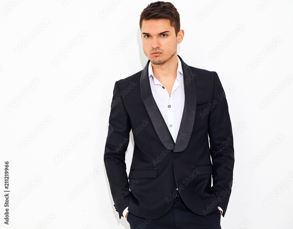 portrait of handsome fashion stylish hipster lumbersexual businessman model dressed in elegant black classic suit posing near white wall in studio. Metrosexual portrait of handsome fashion stylish hipster lumbersexual businessman model dressed in elegant black classic suit posing near white wall in studio. Metrosexual