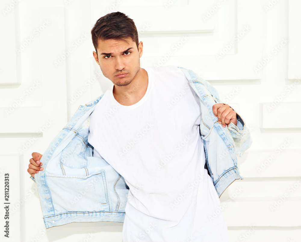 Portrait of handsome young model man dressed in jeans clothes posing near white textured wall