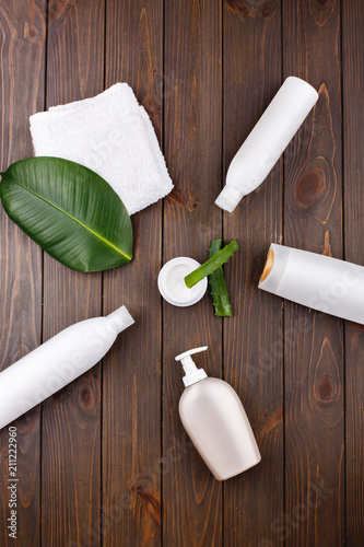 White towel, bottles of shampoo and conditioner lie on a table with green leaf and aloe