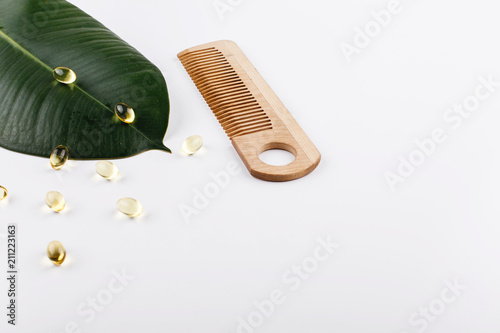 Large green leaf , wooden comb and capsules with oil lie on white table