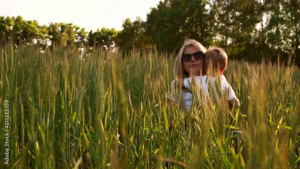 Loving mom and son hugging and playing with a soccer ball in a field with spikelets in beautiful sunset light in white t-shirts Loving mom and son hugging and playing with a soccer ball in a field with spikelets in beautiful sunset light in white t-shirts