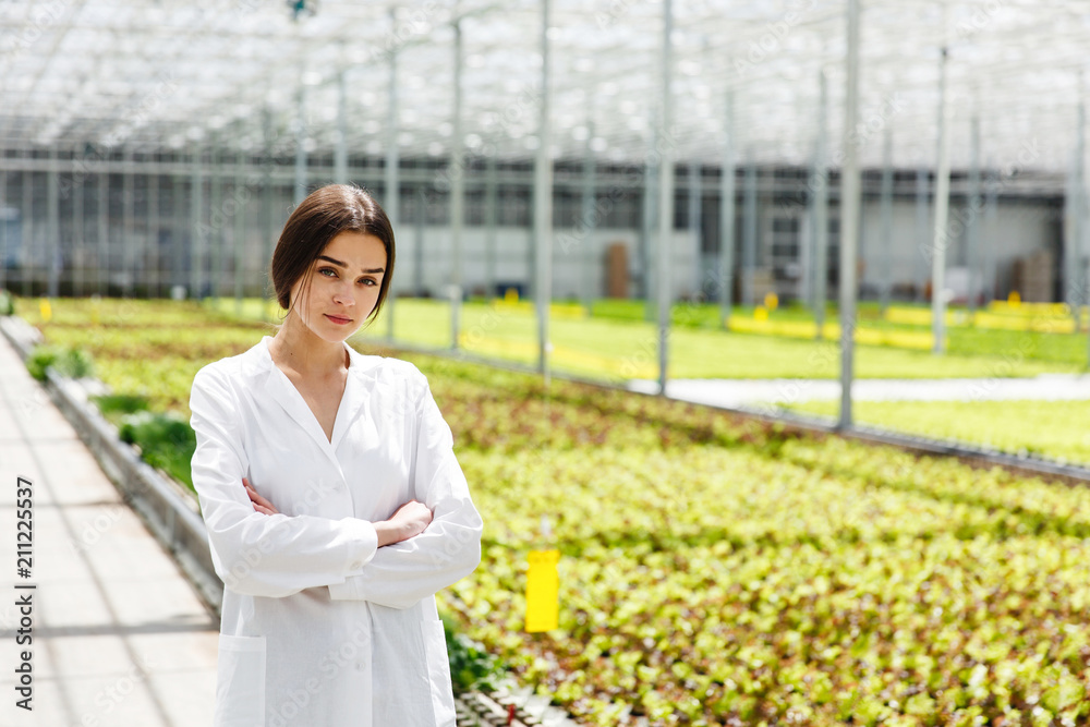 Woman in white laboratory robe stands before plants in the greenhouse Woman in white laboratory robe stands before plants in the greenhouse