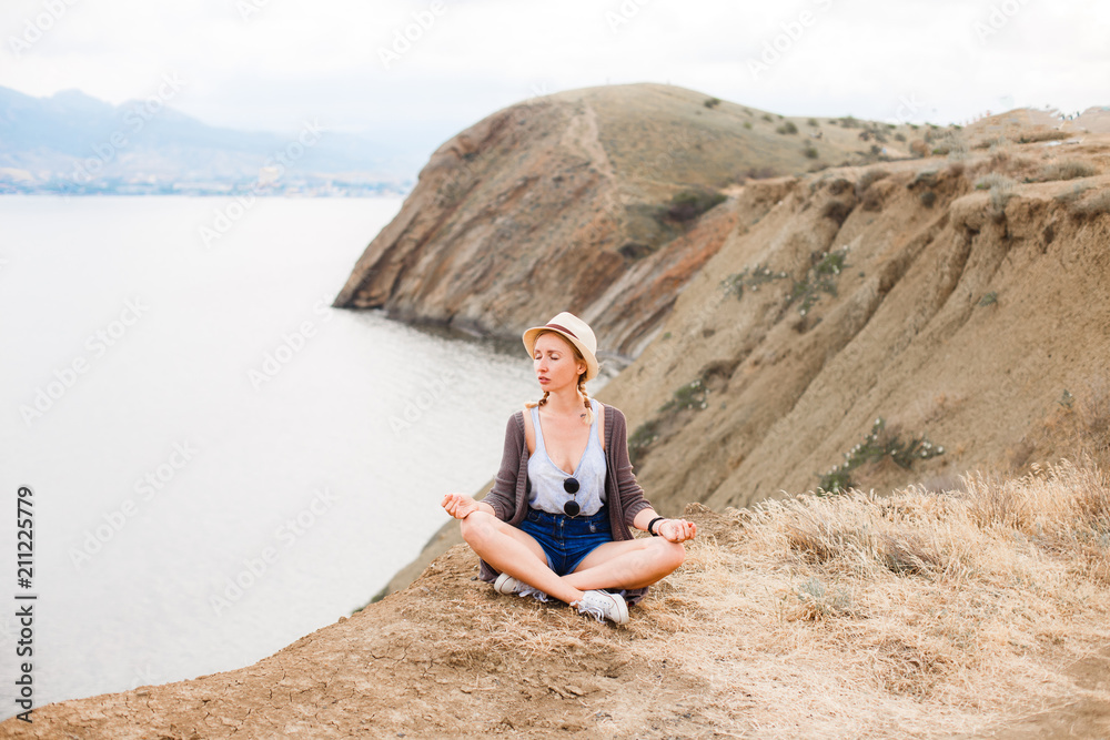 The girl is meditating on the edge of the cliff above the sea.