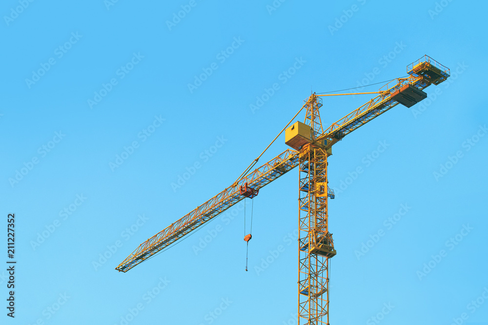 Simple yellow tower crane at construction site on blue evening sky background Simple yellow tower crane at construction site on blue evening sky background
