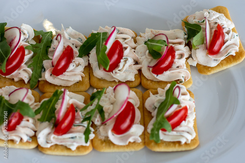  Colorful sandwiches with cheese paste on crackers decorated with radish tomato and arugula on a white plate
