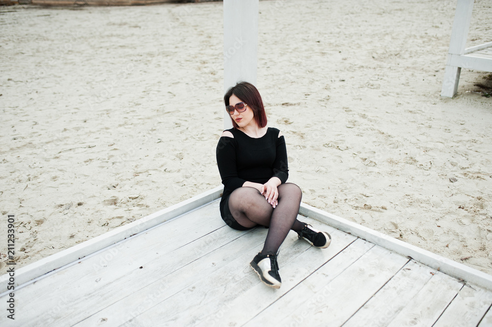 Portrait of brunette girl in black dress sitting at white wooden construction. Portrait of brunette girl in black dress sitting at white wooden construction.