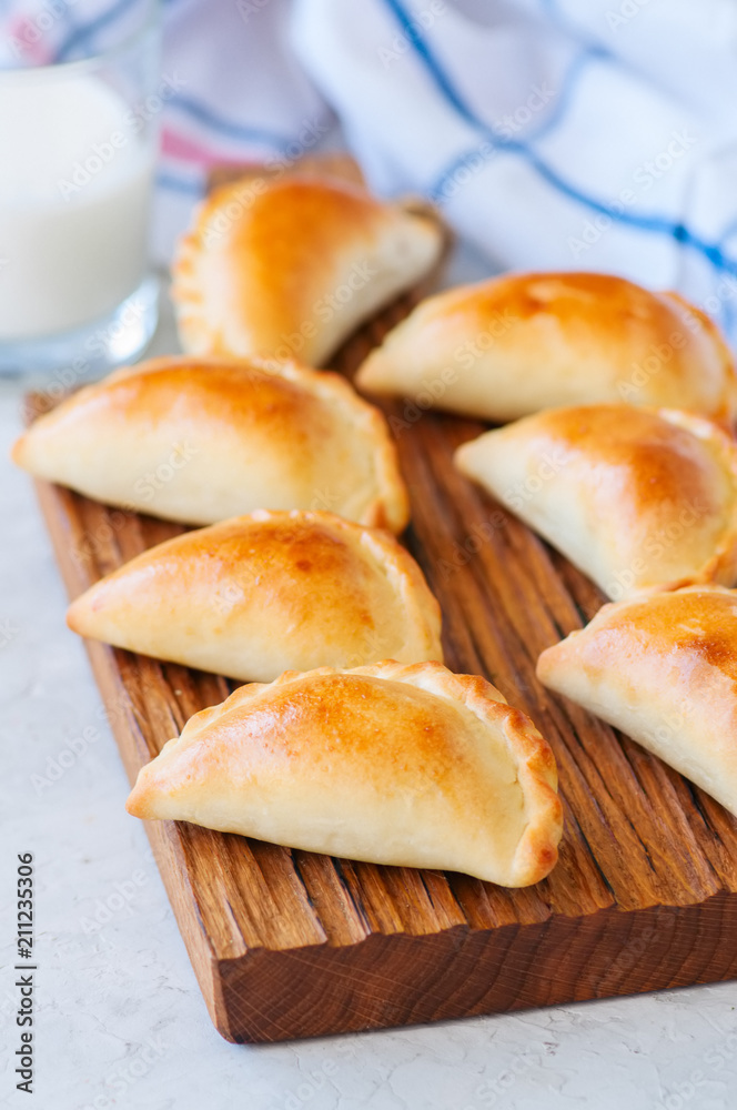 Homemade potato stuffed empanadas on a wooden board. White stone background. Homemade potato stuffed empanadas on a wooden board. White stone background.