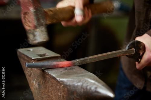 Close-up of a blacksmith's hands manipulating a metal piece above his forge, selective focus.