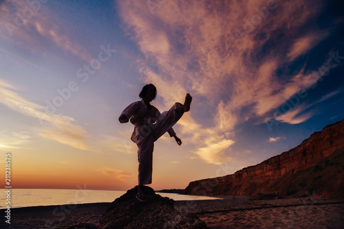 Silhouette of a samurai in a kimono while training on the ocean coast, at sunrise. The concept of a healthy lifestyle, unity with nature, meditation. 