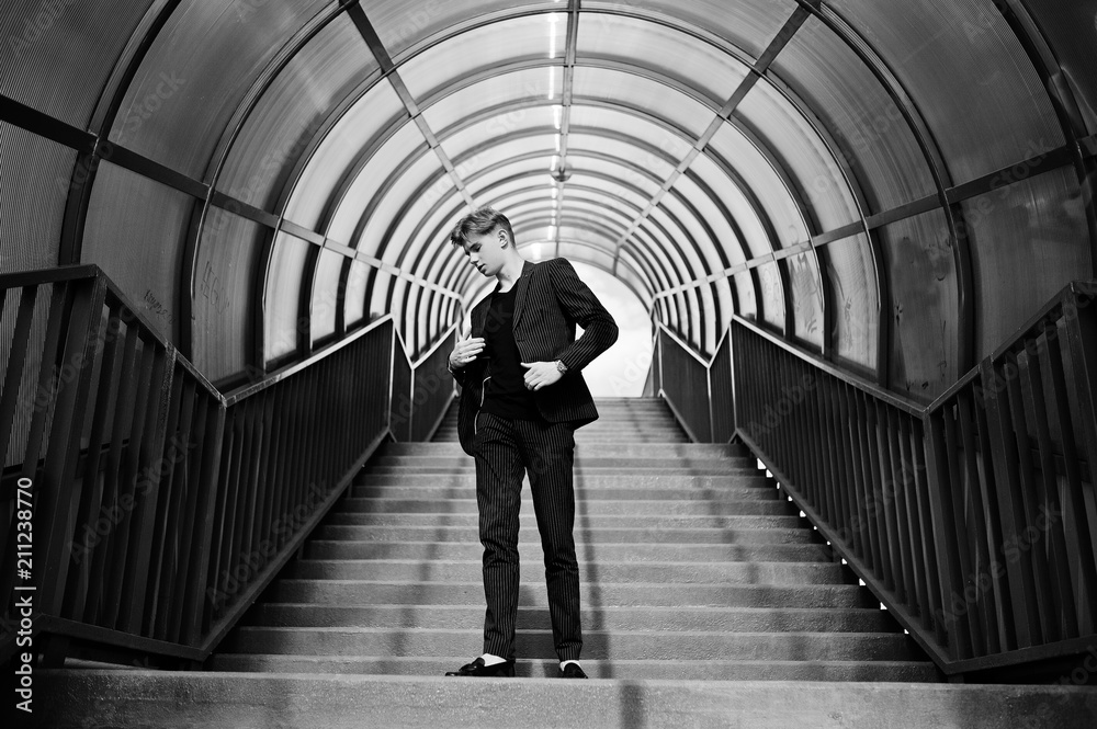 Young stylish macho boy in black jacket posed outdoor of street. Amazing model man at red stairs tonnel.