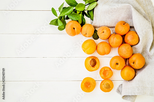 fresh apricots scatter with green leaves on white wooden background with a table linen top view
