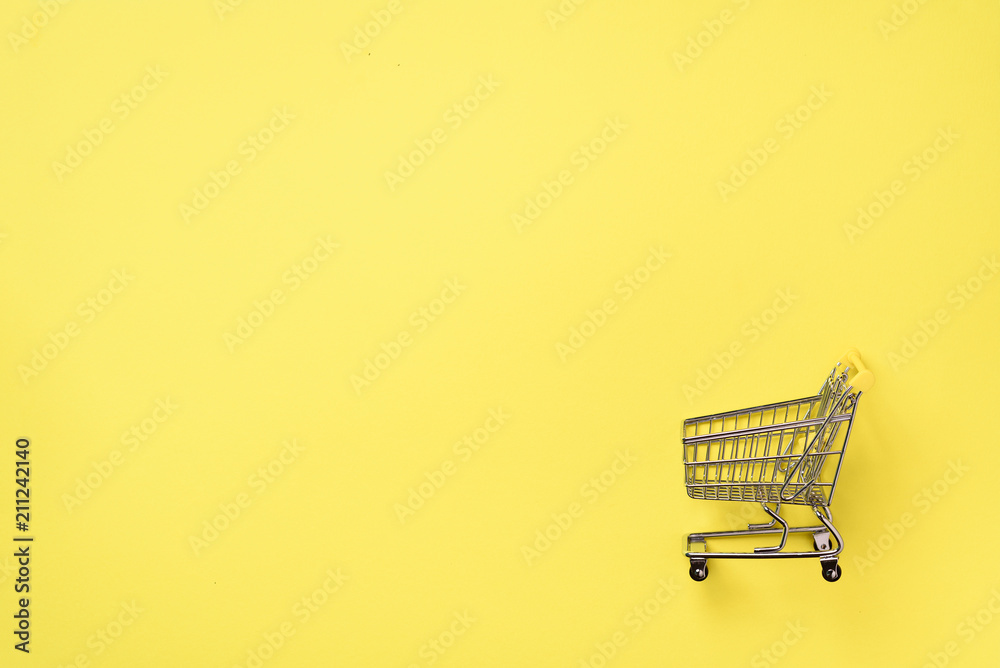 Shopping cart on yellow background. Minimalism style. Creative design. Top view with copy space. Shop trolley at supermarket. Sale, discount, shopaholism concept. Consumer society trend Shopping cart on yellow background. Minimalism style. Creative design. Top view with copy space. Shop trolley at supermarket. Sale, discount, shopaholism concept. Consumer society trend