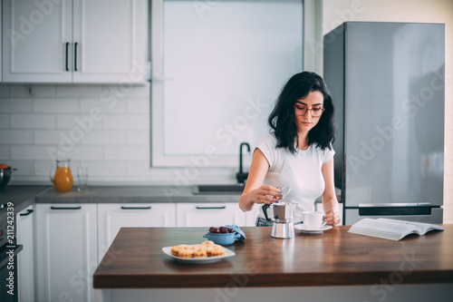 Beautiful young woman pouring coffee in the kitchen © Suteren Studio