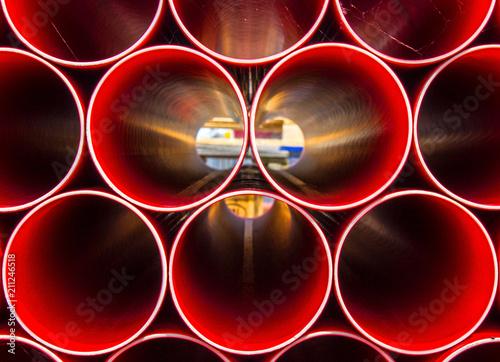 Stack of Red Construction pipes, the symmetry of evenly spaced pipework except for one pipe standing out slightly