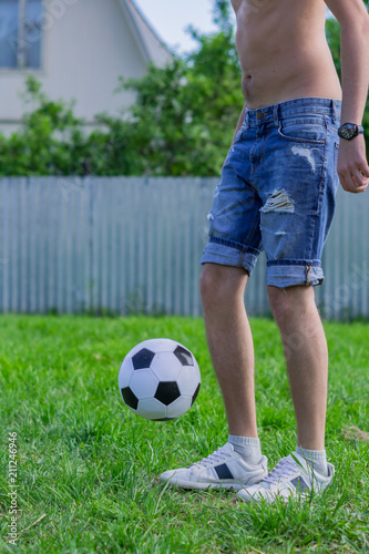 young man in denim jeans and white sneakers playing football ball outdoors. Amateur football player mint the ball © IKvyatkovskaya