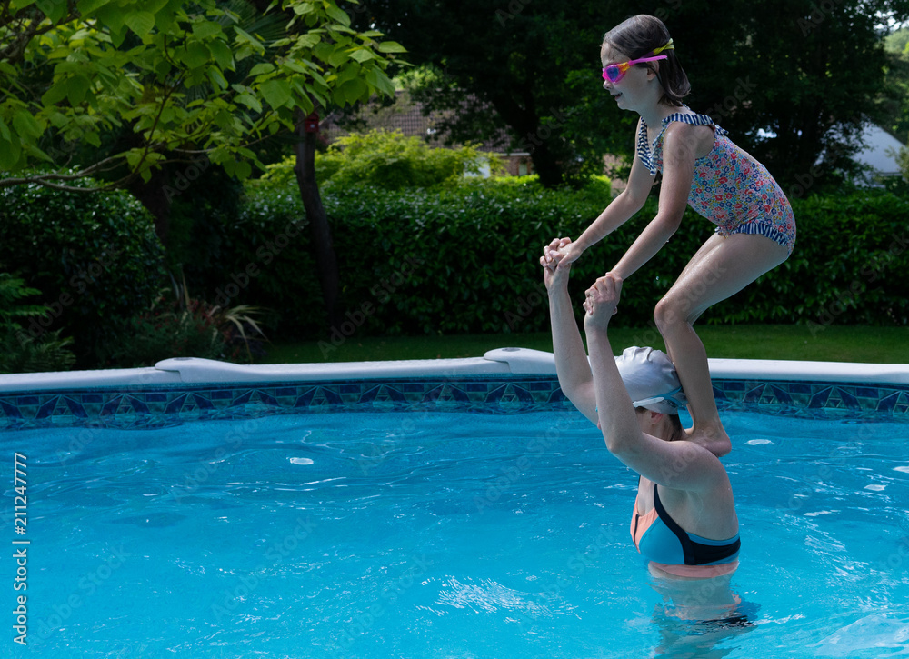 Mother and daughter in the swimming pool with daughter standing on shoulders about to jump in