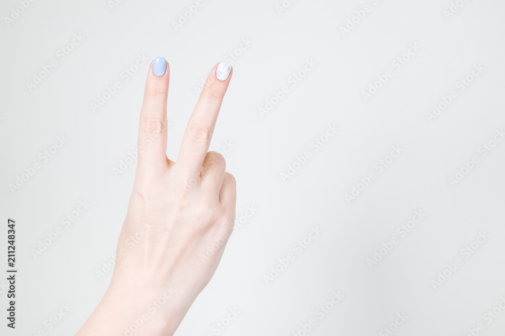 Closeup view of white female hand in victory gesture isolated on white background. Fingernails with modern gel polish manicure of white and blue colors. Closeup view of white female hand in victory gesture isolated on white background. Fingernails with modern gel polish manicure of white and blue colors.