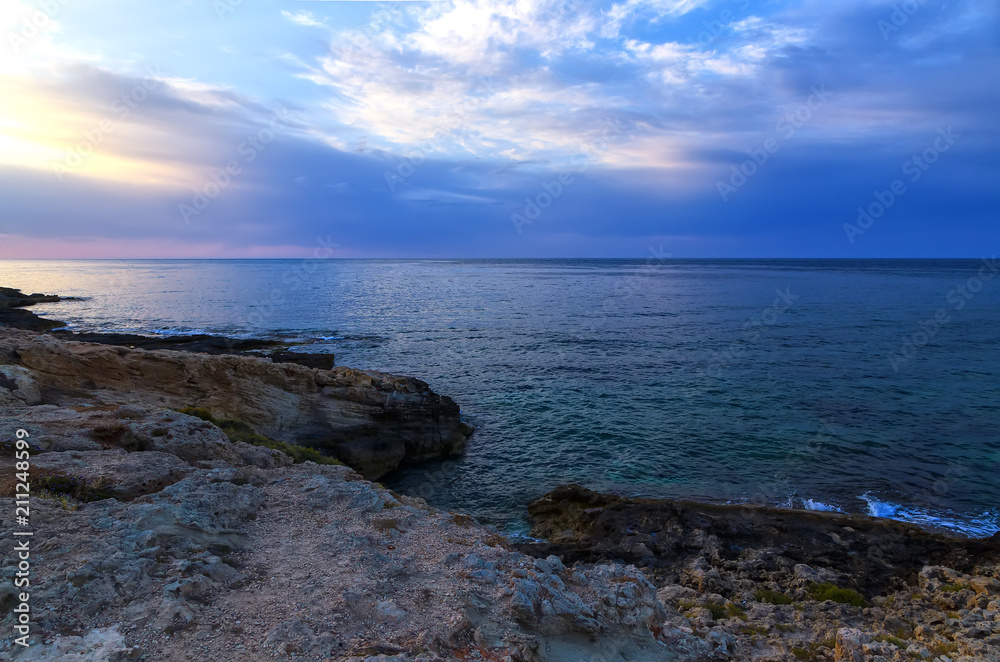 Bright colorful sunset on sea with beautiful clouds and with puddles in volcanic rock in the foreground