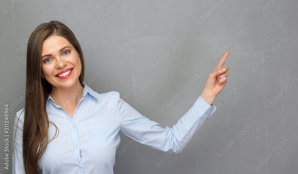 Smiling woman pointing finger to copy space on gray wall. Smiling woman pointing finger to copy space on gray wall.