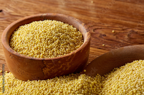 A wooden dish with millet on rustic wooden background, top view, close-up, selective focus.