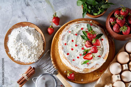 Strawberry tart covered with whipped sour cream surrounded by organic ingredients over white background, flat lay. photo