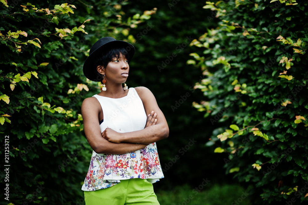 Amazing african american model woman in green pants and black hat posed at park. Amazing african american model woman in green pants and black hat posed at park.