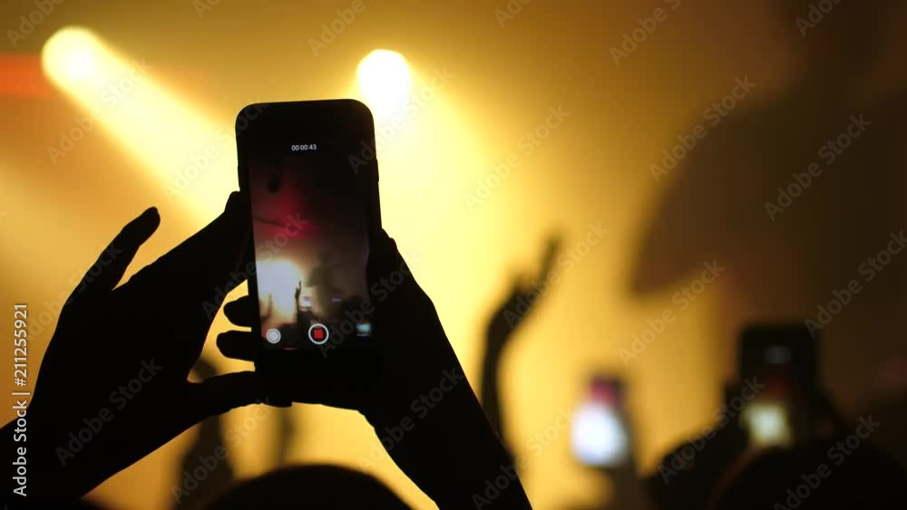 Spectator hands silhouette in concert stage light holds up in air shoot mobile phone video of performance