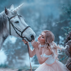 A fairy in a tender vintage dress hugs a unicorn. Fantastic magical, radiant horse. Background river and forest. Blonde girl with wavy hair - light elf. Artistic Photo