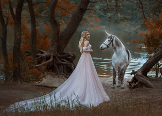 The princess met a unicorn in the forest. The blonde girl with a gentle make-up, is dressed in a long vintage dress with a lush skirt and train. Artistic Photo