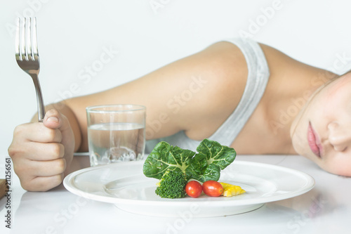 unhappy asian women is on dieting time looking at broccoli on the fork. girl do not want to eat vegetables and dislike taste of broccoli.